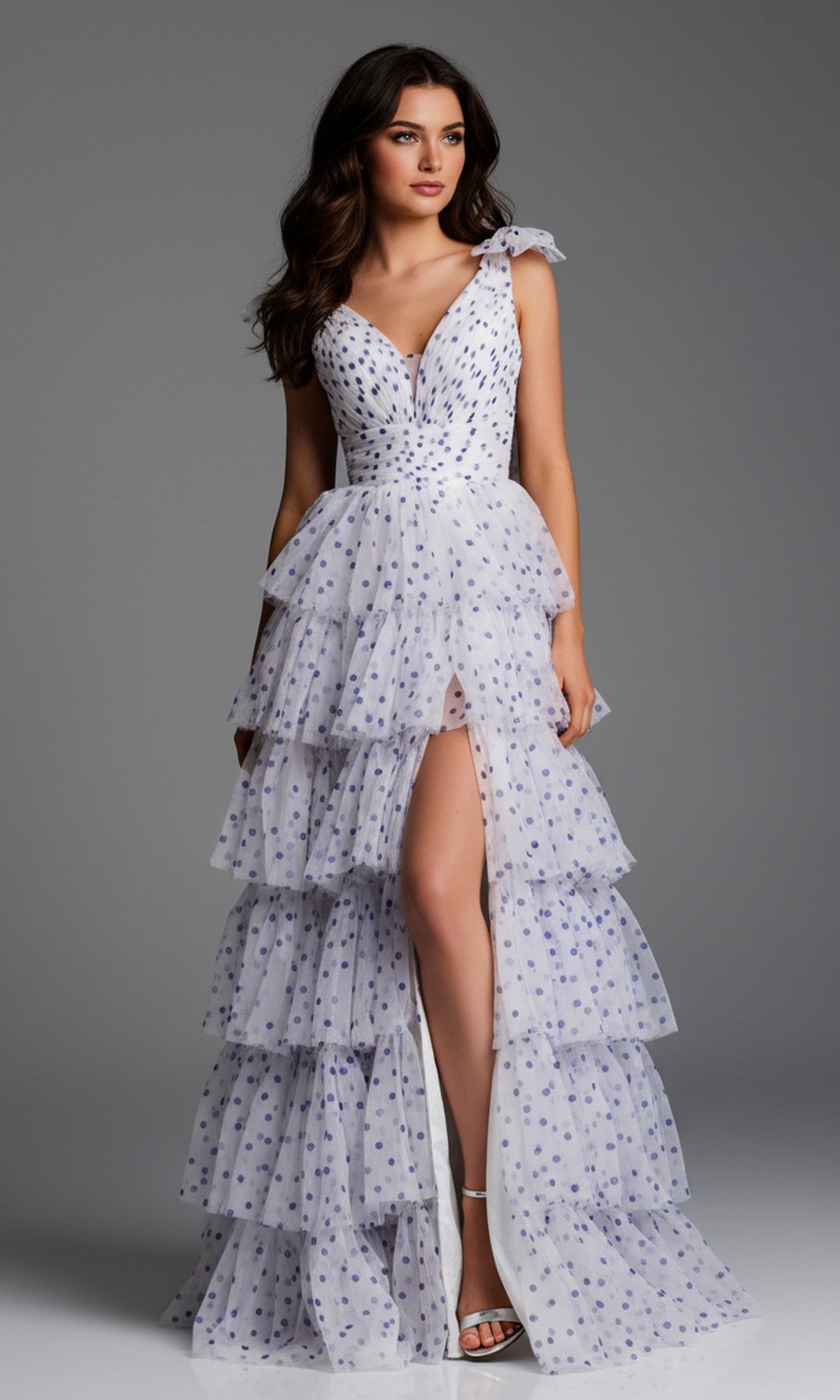 A woman wearing the Jovani 49358 long prom dress in off white/purple with a deep V-neck, tiered tulle, polka dots, and a high slit stands against a plain gray background.